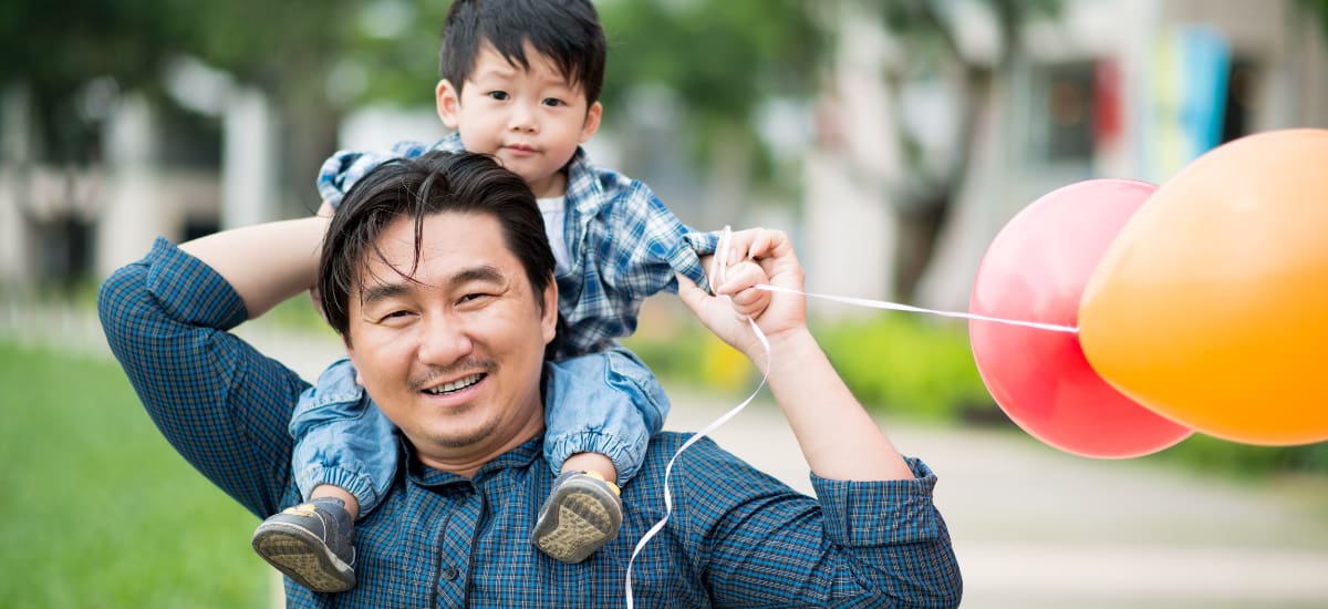 Father carrying his toddler on his shoulders, with balloons