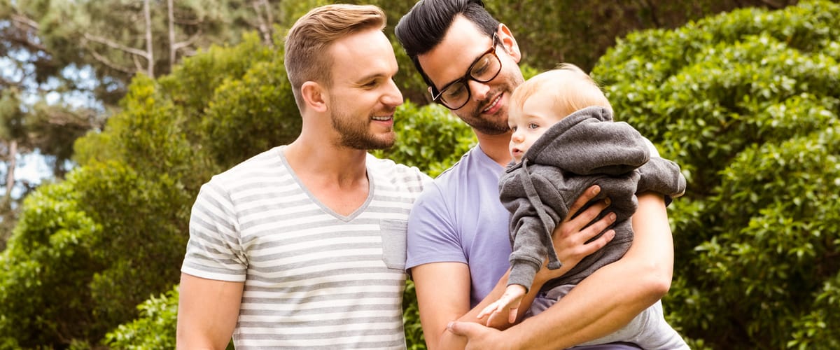 Two dads holding their toddler-aged child at the park