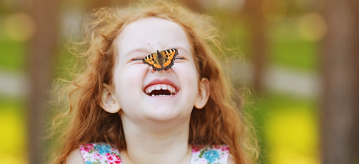 Young girl laughs as a butterfly lands on her nose