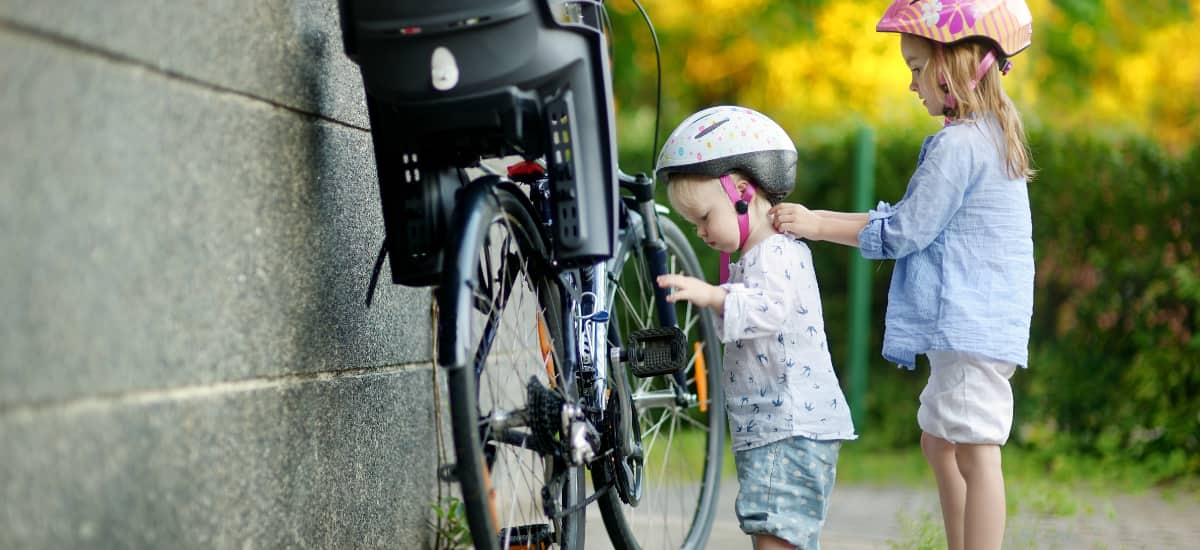 A young girl adjusts a bike helmet on her younger sister