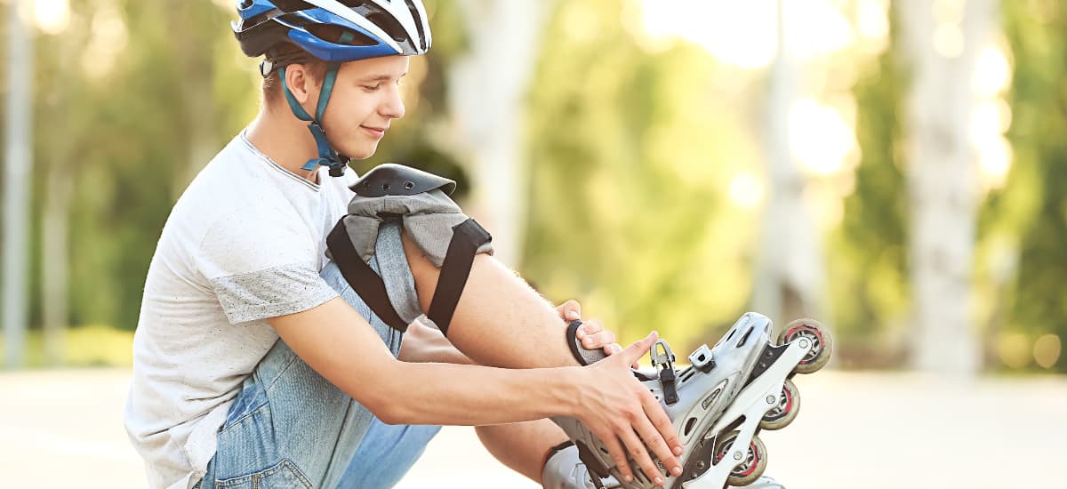 A teen boy sits on the ground and adjusts the buckle on his roller blade