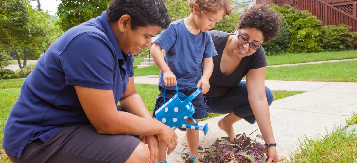 Two moms watering plants with their son