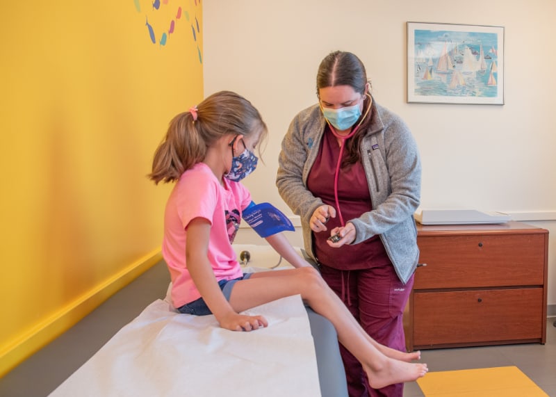 A nurse takes the blood pressure of a young girl in a bright exam room