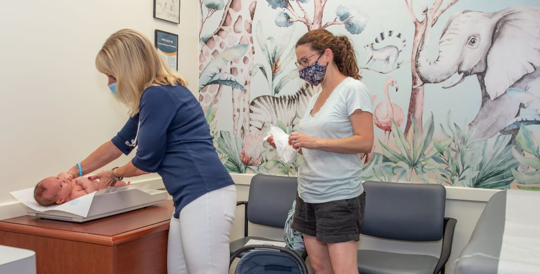 A doctor weighs an infant in an exam room while the baby's mother looks on